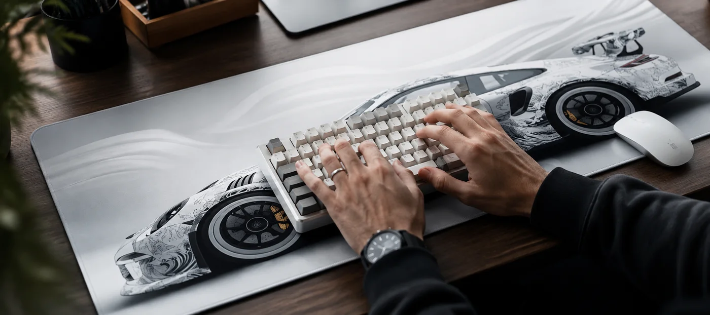 Hands typing on a white mechanical keyboard resting on a light grey XXL desk mat printed with a white sports car, white mouse on the right
